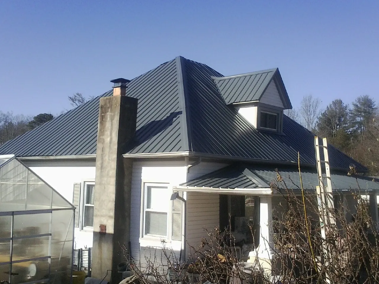 Dark blue standing seam metal roof on a white farmhouse with dormer — Slate & Tile Roof Repair by Roofing Brothers in Carmel Valley