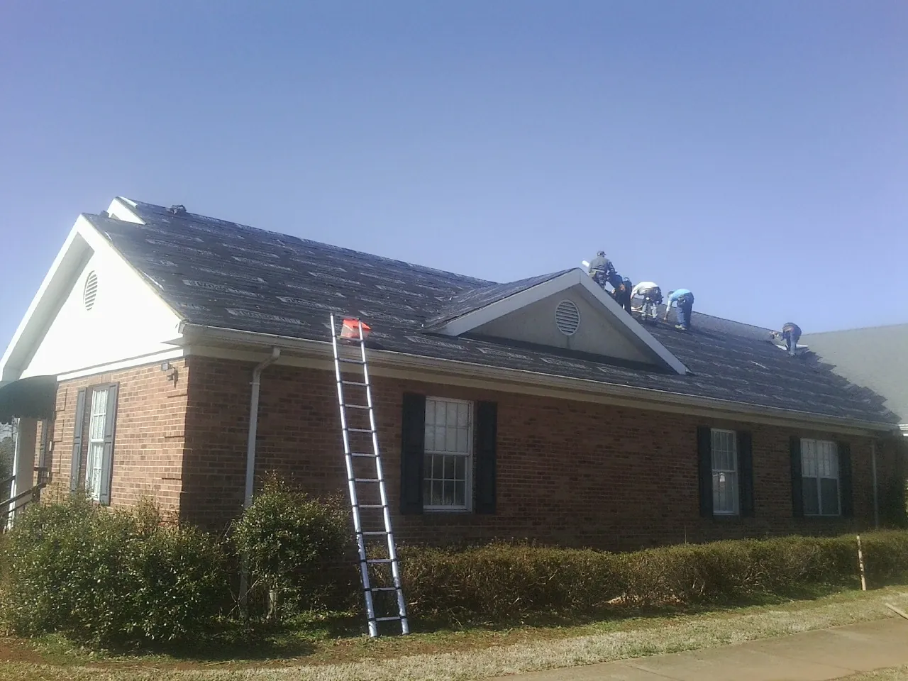 Crew tearing shingles off a brick ranch roof with a ladder set — Metal Roof Repair work by our crew in Carmel Valley