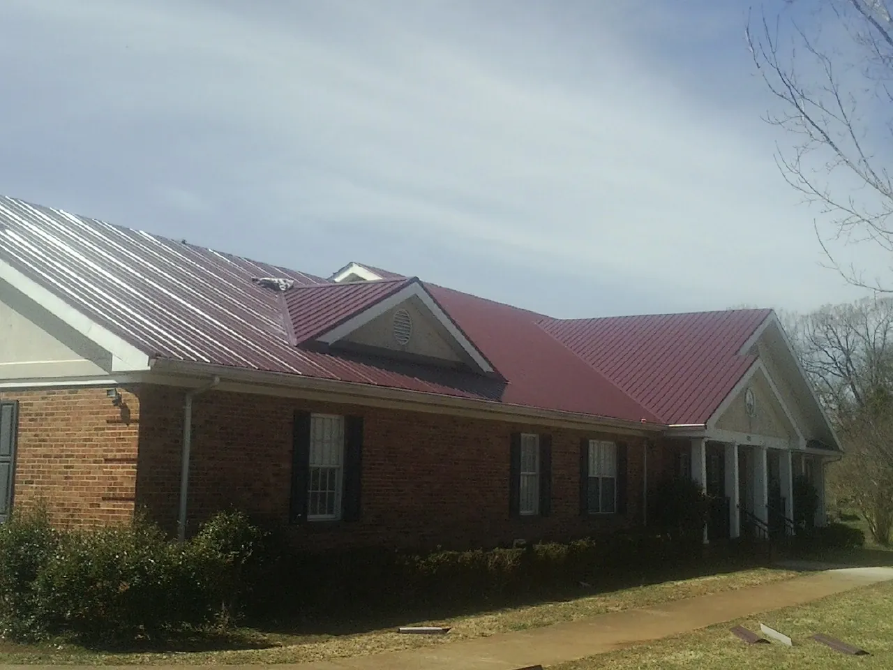 Red metal roof with gabled entries on a long brick building, from a Hail Damage Roof Repair job in Carmel Valley