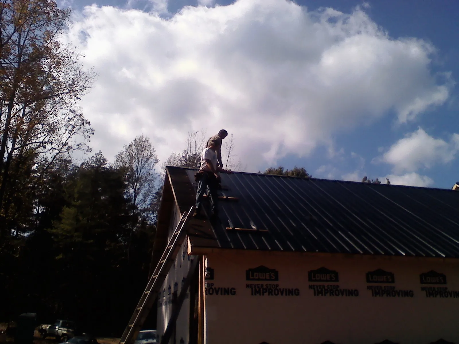 Roofer fastening dark metal panels high against a cloudy sky, from a Roof Inspection job in Carmel Valley